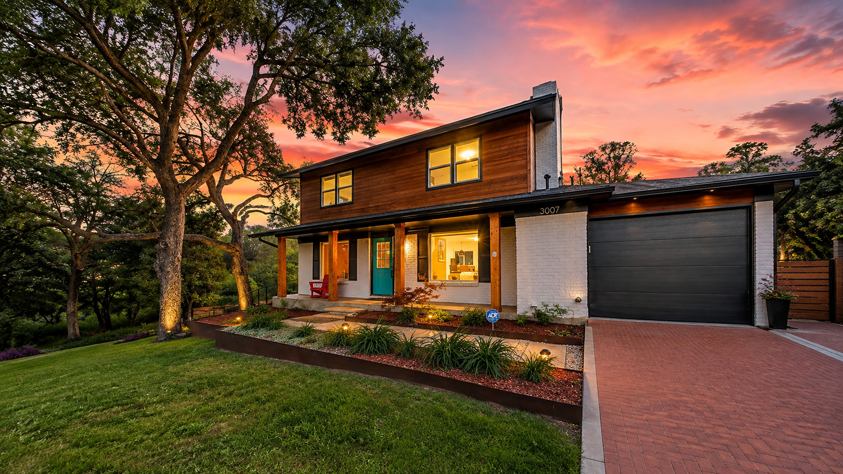 Two-story modern house at sunset with a brick driveway and illuminated foyer door under a covered porch.